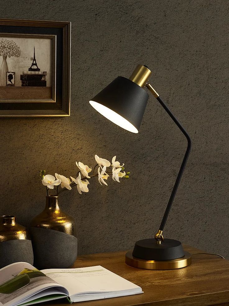 a desk lamp sitting on top of a wooden table next to a vase with flowers