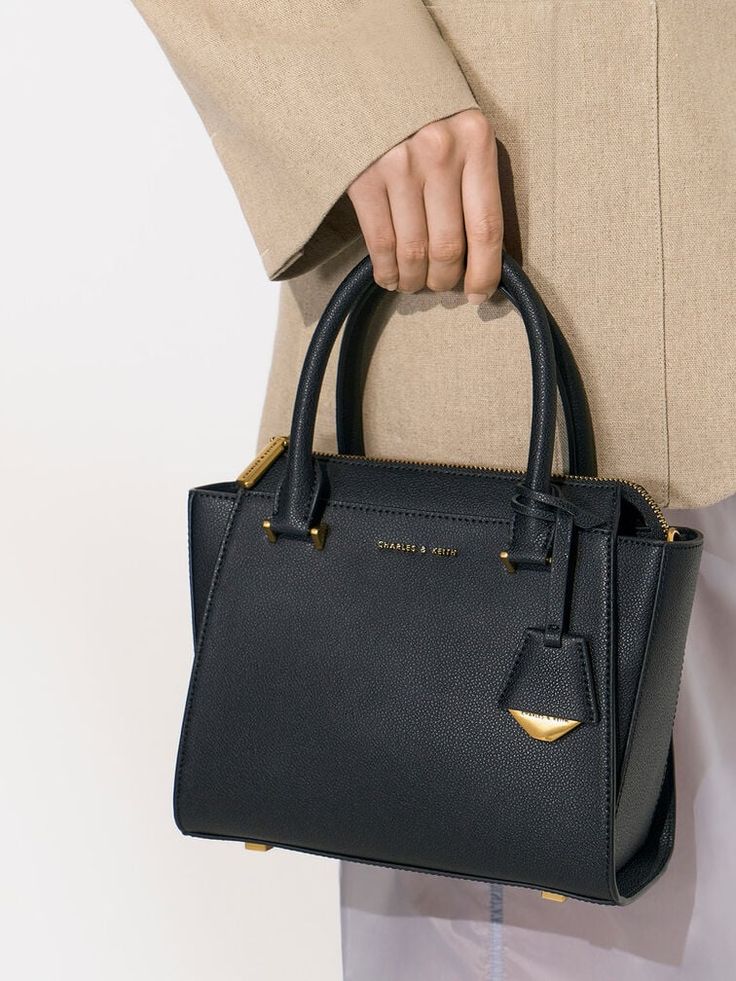 This product is made with at least 20% sustainable materials by weight. CHARLES & KEITH uses recycled, degradable, organic, and water-based materials in our eco-conscious collection. Keep things simple and stylish with this Harper top handle bag. In match-all black to complement any outfit, this bag features striking gold-toned hardware that will add a hint of shine to your overall look. Carry it by the sturdy double handles or clip on the adjustable strap to turn it into a crossbody bag and keep your hands free. Structured and sophisticated, this versatile accessory works perfectly with office ensembles and off-duty outfits alike. Off Duty Outfits, Geometric Top, Brand Collaboration, Charles Keith, Black Tote Bag, Handle Bag, Hands Free, Clip On, All Black