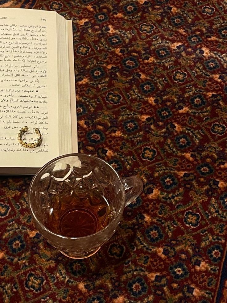 an open book with a ring on it next to a glass mug