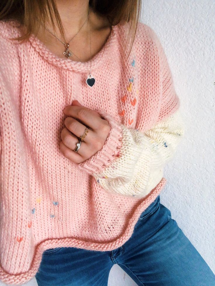 a woman wearing a pink sweater and blue jeans with her hand in her pocket,