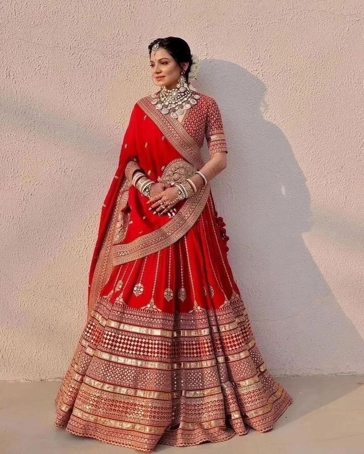 a woman in a red and gold bridal gown standing next to a white wall