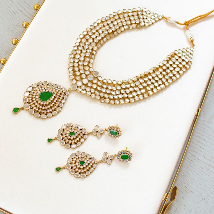 An heirloom of divinity, crafted through the ages! Introducing an opulent fiver-layer kundan mala, adorned with a magnificent emerald stone centerpiece that exudes timeless elegance, this set blends the regal charm of kundan with the vibrant allure of emeralds. A masterpiece of craftsmanship, it promises to elevate any occasion with its majestic allure. The listing includes long mala and a pair of matching earrings. Gold-plated on high-quality brass as base metal. Made by order. Kindly allow 5-7 Spiritual Kundan Gemstone Necklace, Spiritual Kundan Necklace With Gemstone For Festive Season, Emerald Kundan Necklace With Intricate Design For Festive Occasions, Festive Emerald Kundan Necklace With Intricate Design, Festive Emerald Kundan Chandbali Necklace, Festive Chandbali Kundan Necklace With Emerald, Festive Emerald Kundan Necklace With Stone Work, Green Chandbali Bridal Necklace For Rituals, Festive Spiritual Kundan Necklace For Wedding