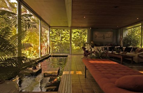 a living room filled with lots of windows next to a small pond and couches