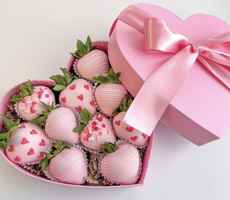 a heart shaped box filled with chocolate covered strawberries and a pink bow on top