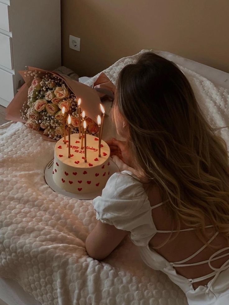 a woman laying in bed next to a cake with lit candles on top of it