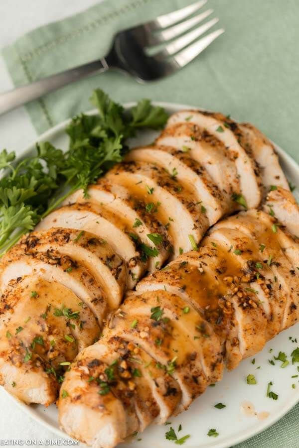 sliced chicken on a white plate with parsley and green garnish next to a fork