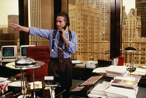 a man standing in an office with headphones on and pointing at something while talking on the phone