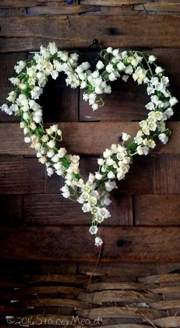 a heart shaped wreath with white flowers hanging on a wooden wall