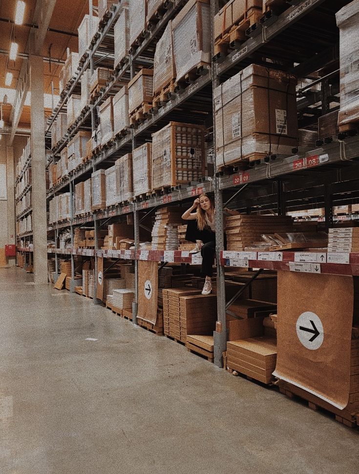 a woman is standing in the middle of a large warehouse filled with boxes and shelving