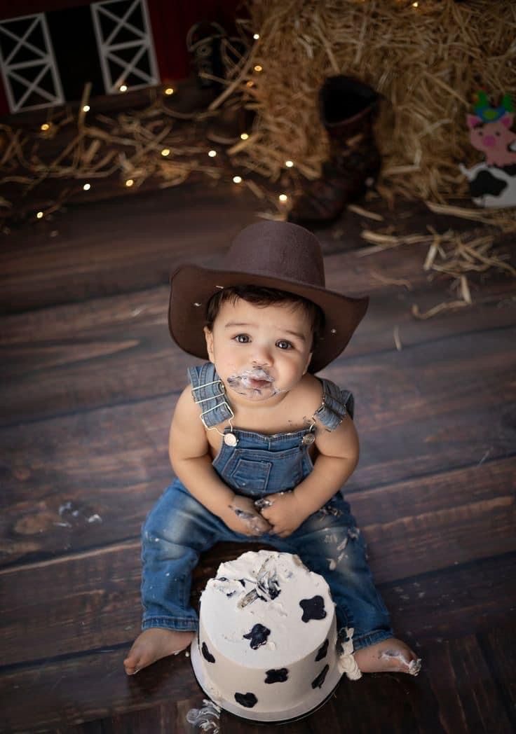 a little boy sitting on top of a wooden floor next to a cake with frosting