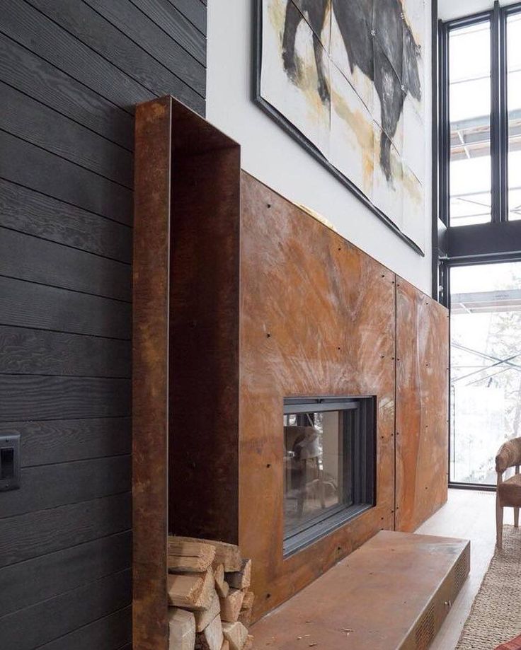 a fireplace in a living room with wood stacked on the floor and framed pictures above it