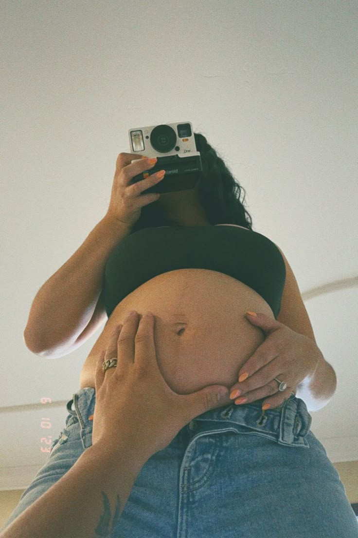 a pregnant woman taking a selfie with her camera in front of her belly,