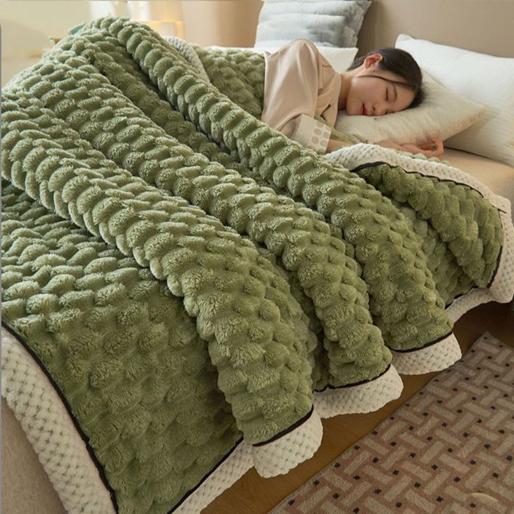 a woman laying in bed under a green blanket