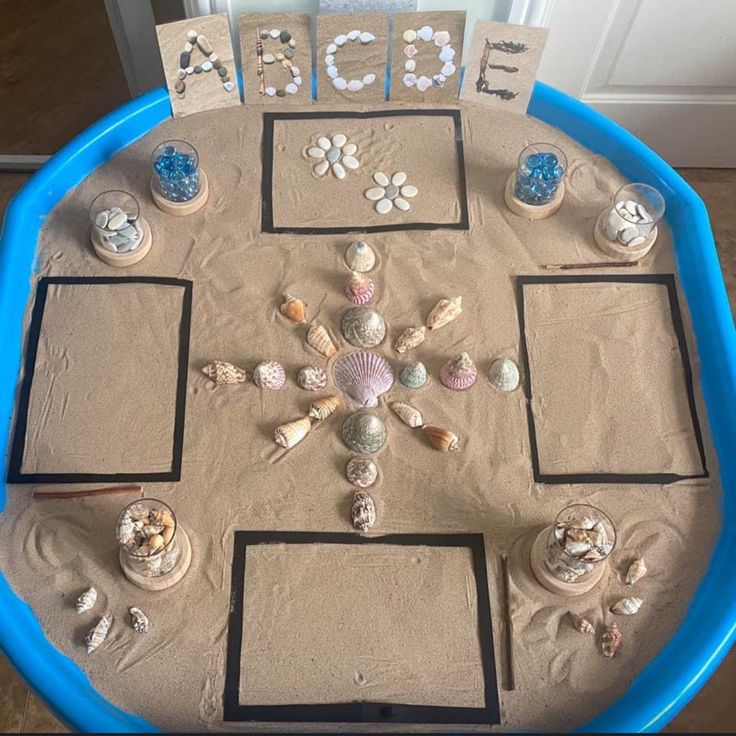 there is a sand tray with sea shells on it and letters that spell out the word beach