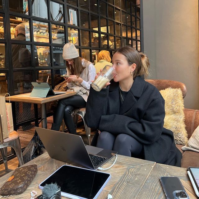 a woman sitting on a couch drinking from a bottle while looking at her laptop computer