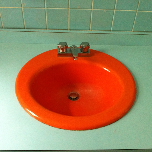 an orange sink with two faucets on top of it in a blue tiled bathroom