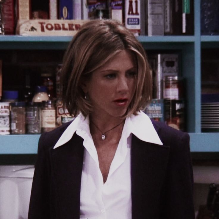 a woman in a white shirt and black blazer standing in front of a book shelf