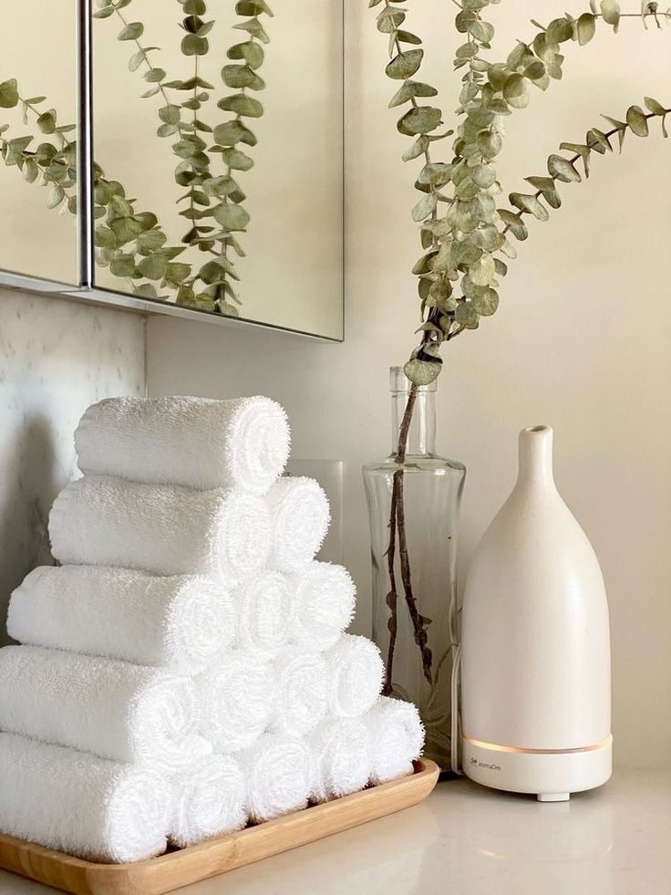 white towels are stacked on a tray next to a vase with flowers and a mirror in the background