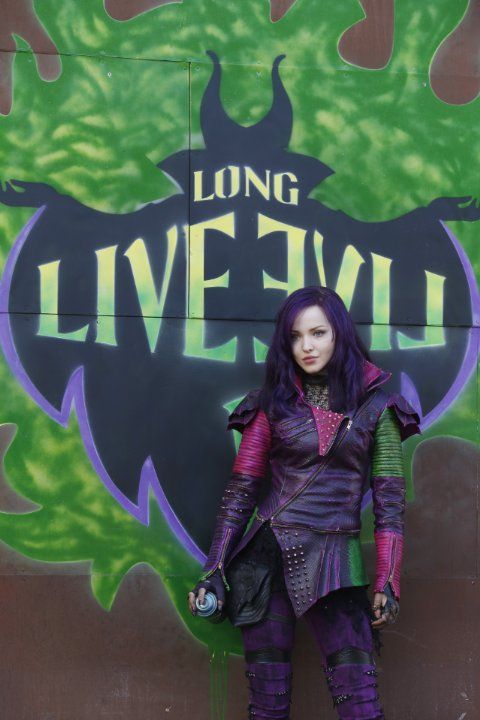 a woman with purple hair standing in front of a green and black sign that says live evil