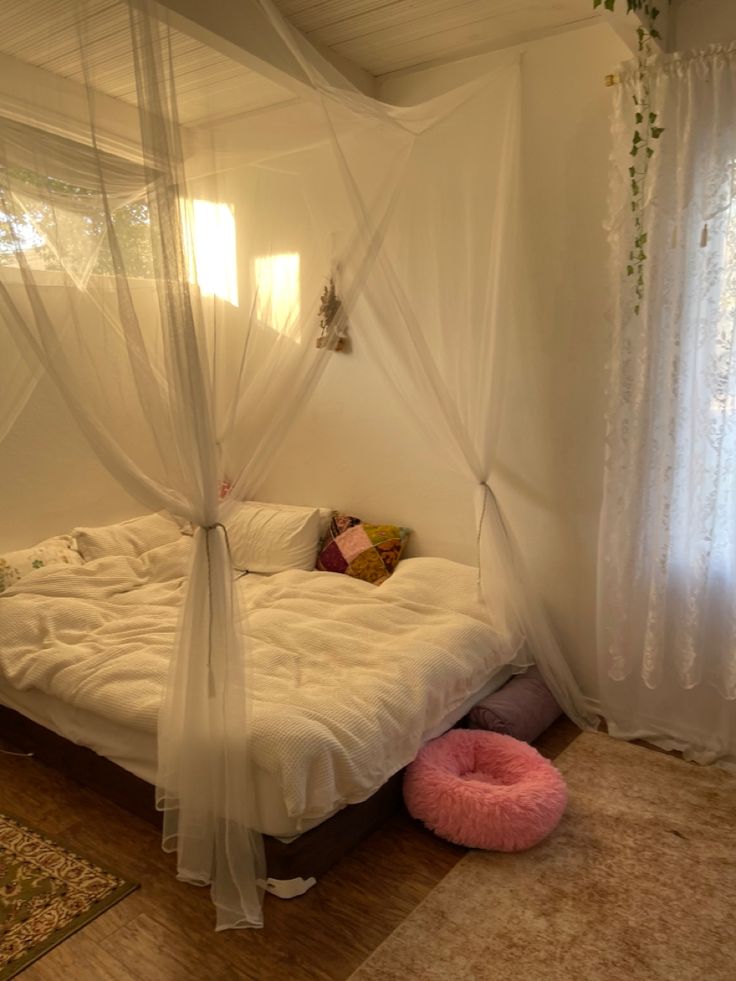 a bed with white sheets and mosquito netting over it, in a room with wooden floors