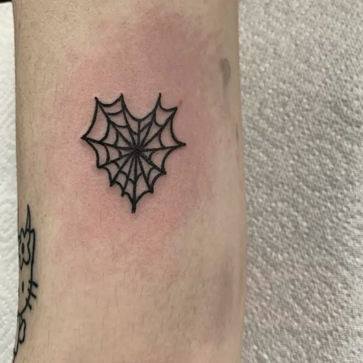 a small spider web tattoo on the left arm and leg, it is black in color