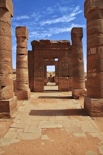 the entrance to an ancient building with columns and pillars on either side, in front of a bright blue sky