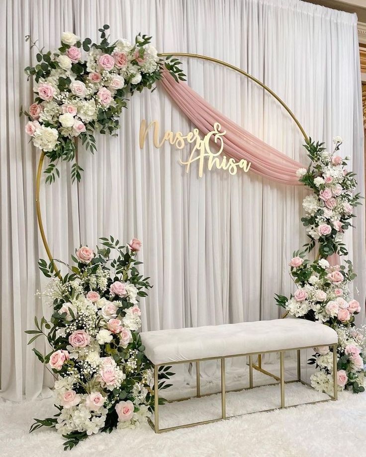 a wedding ceremony setup with pink and white flowers, greenery and a gold arch