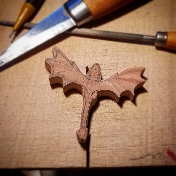 a wooden carving of a bat on a piece of wood next to a pair of scissors