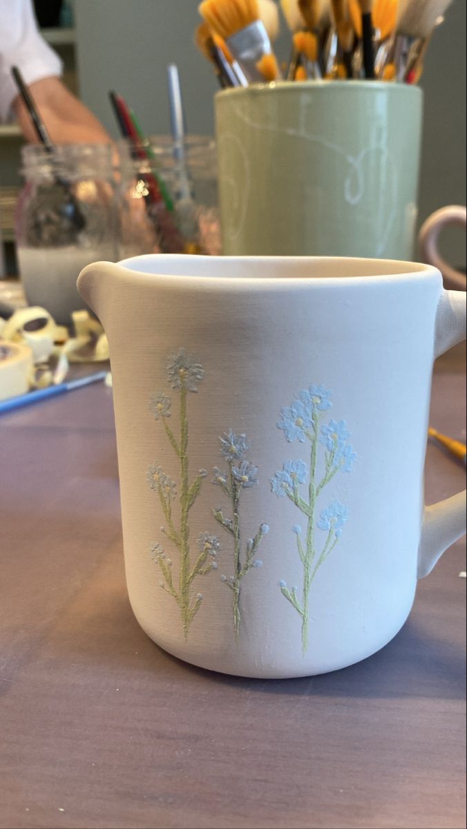 a cup with flowers painted on it sitting on a table next to paintbrushes