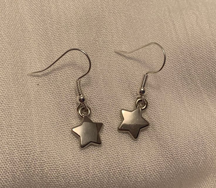 These Dainty, Glistening Silver Star Drop Earrings are the perfect accessory to complement any outfit. Each pair is handmade and produced in very small quantities, so you're guaranteed to have a unique look.                   ❤ Please note that each earring is not perfeclty identical to its counterpart - our jewelry is made entirely by hand,                        so slight variation does occur.    ------------------------------------------------------------------------------------------------------------------------------------------------------------------------- Caring for your jewelry: ❤ Please handle these earrings with care as they are delicate. Our earrings are made to withstand normal wear, but are vunerable to being damaged if extensive pulling/tugging occurs.  ❤ Avoid getting wet Silver Earrings With Star Charm For Everyday, Metal Earrings With Star Charm For Gift, Dainty Star Shaped Nickel Free Jewelry, Everyday Hypoallergenic Star Jewelry, Silver Star Charm Earrings For Everyday, Gift Earrings With Round Star Charm, Gift Round Earrings With Star Charm, Star Shaped Metal Earrings For Gifting, Minimalist Star Shaped Ear Wire Jewelry