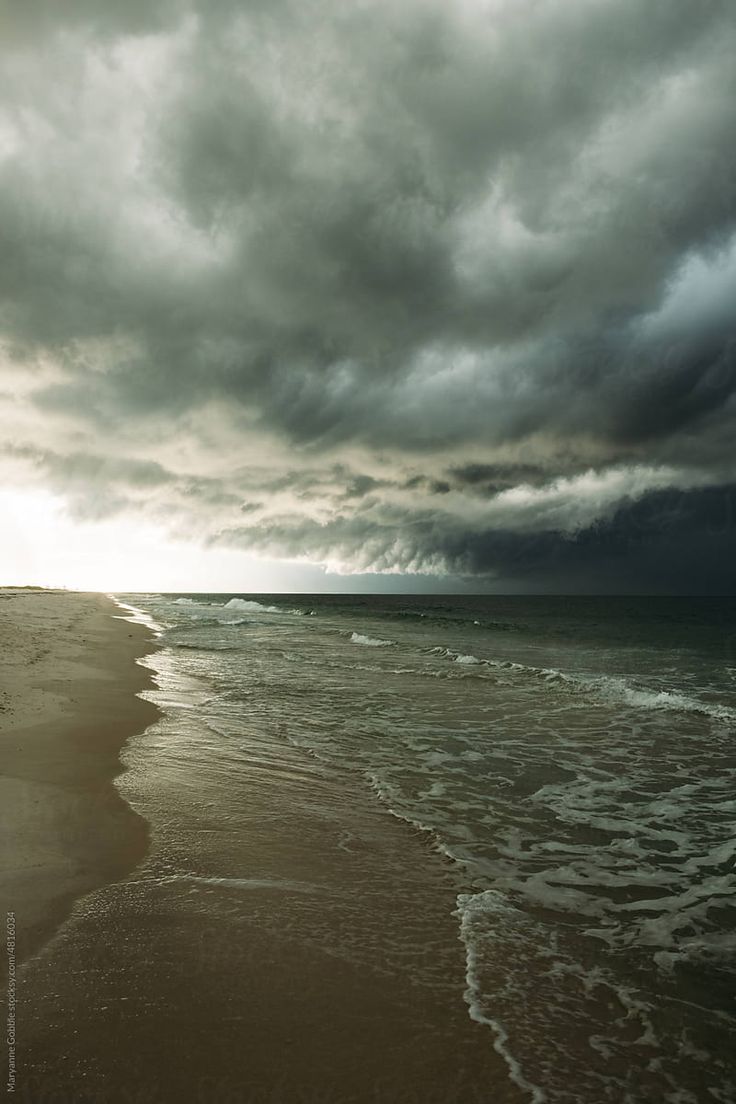 an ocean beach with waves coming in to shore and dark clouds over the water on a cloudy day