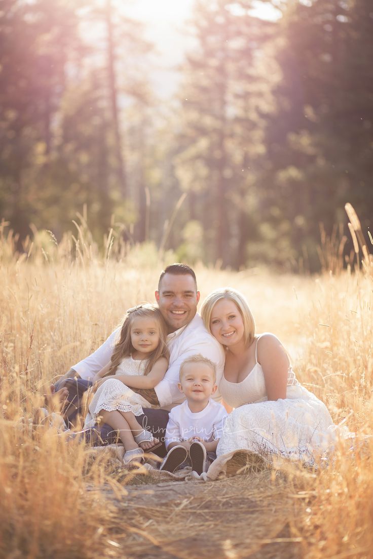 a family is sitting in the middle of a field with tall grass and trees behind them