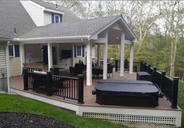 a covered deck with an outdoor hot tub and grill on the other side of it