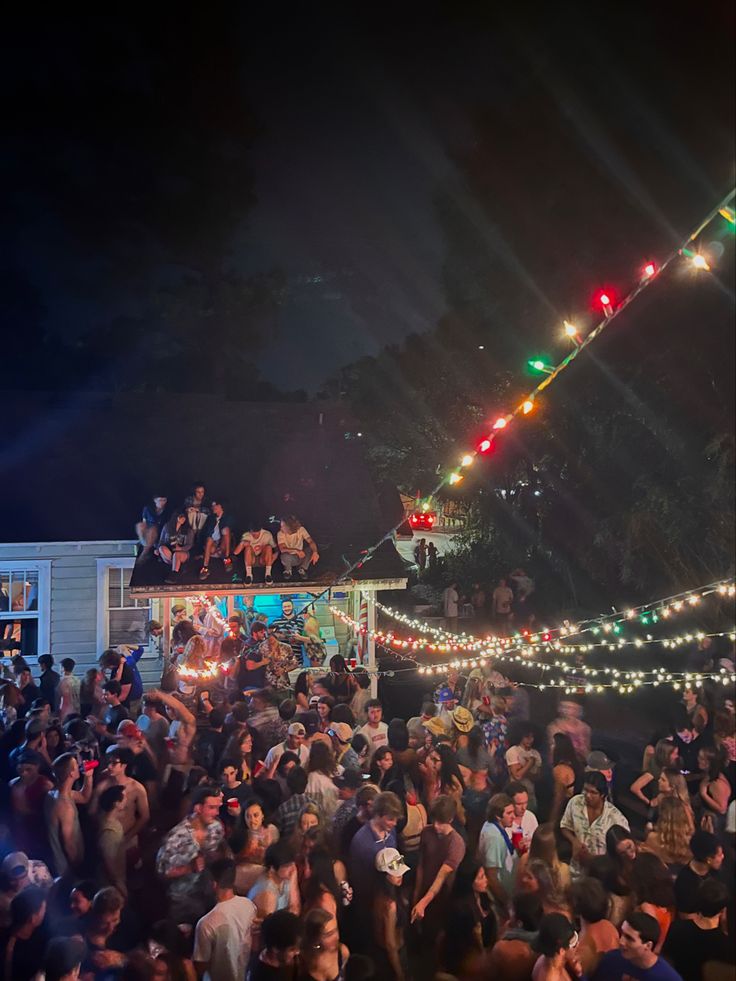 a large group of people standing around each other at night with lights on the roof