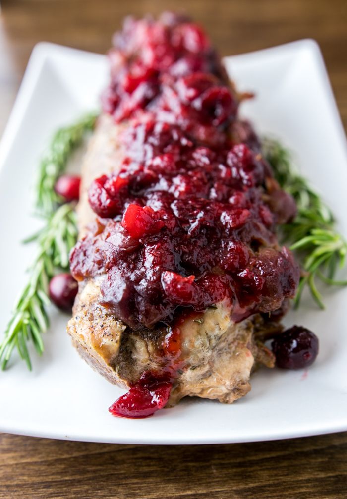 a white plate topped with meat covered in cranberry sauce and garnish