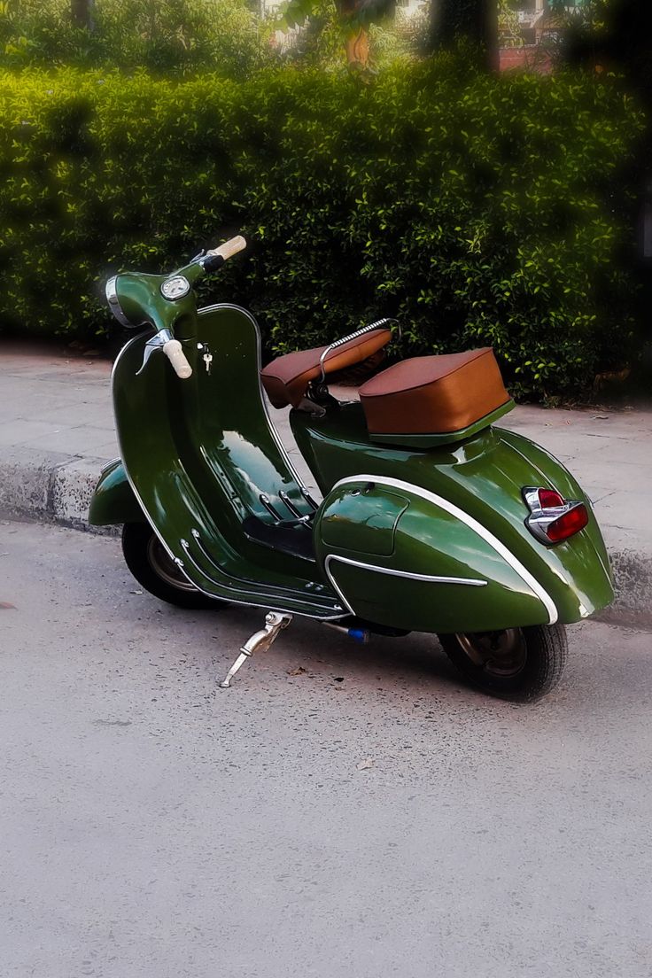 a green scooter parked on the side of the road next to some bushes