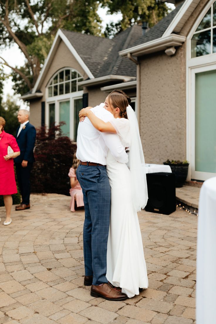 a bride and groom embrace in front of their home as guests walk by onlookers