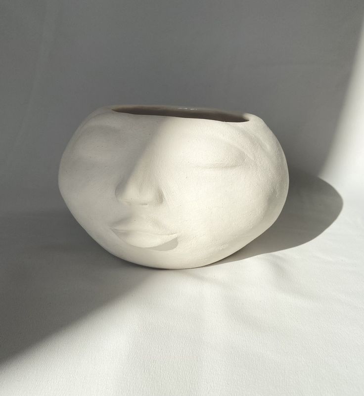 a white vase with a face on it's side sitting against a white background