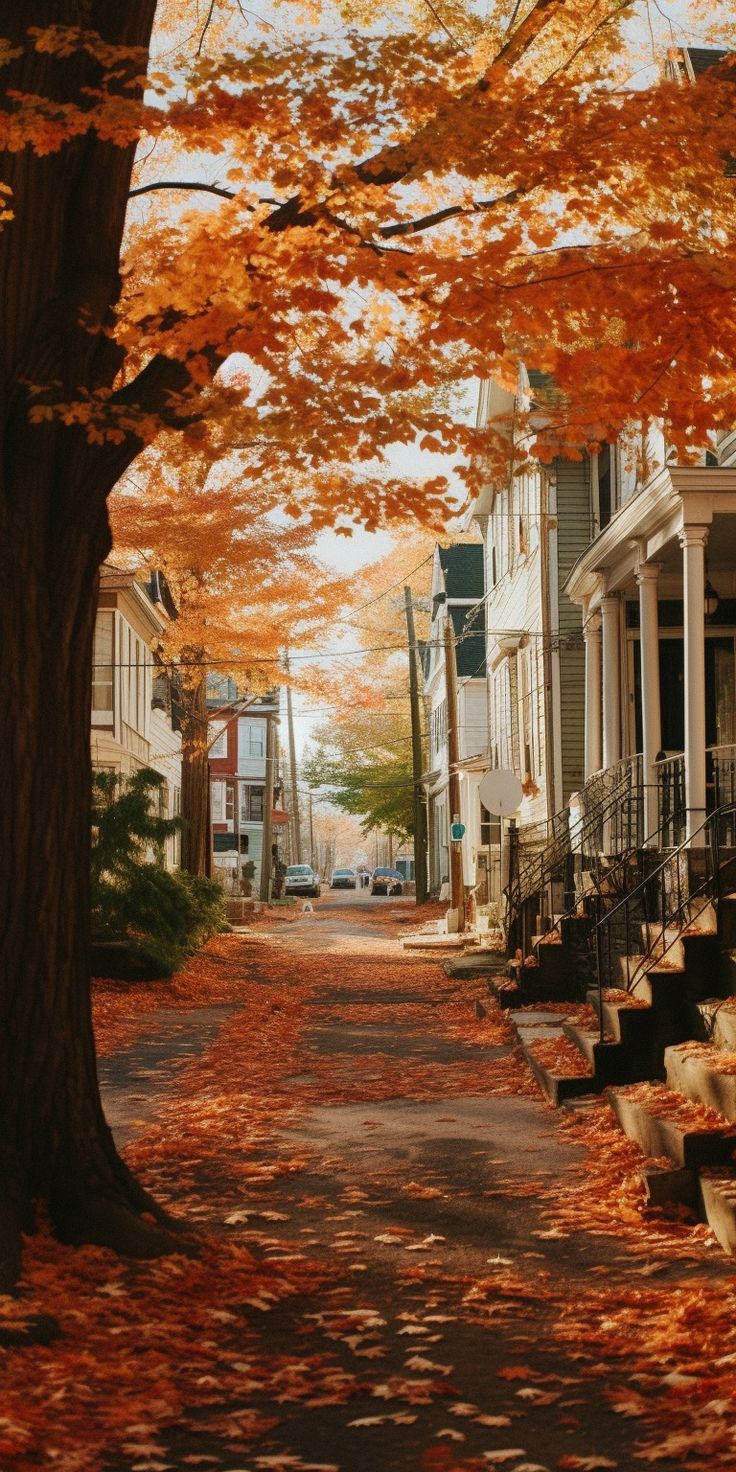 an autumn scene with leaves falling on the ground and trees in front of houses lined with parked cars