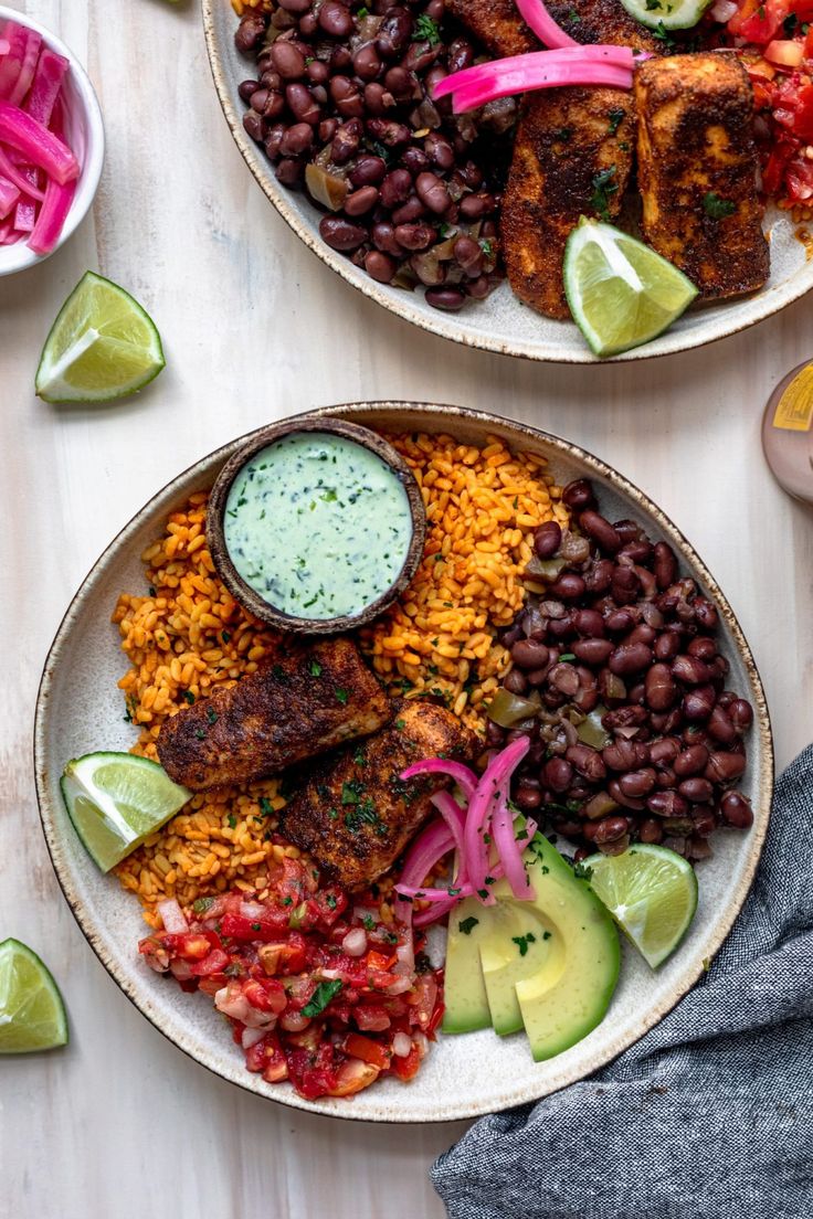 two plates filled with mexican food on top of a wooden table next to lime wedges