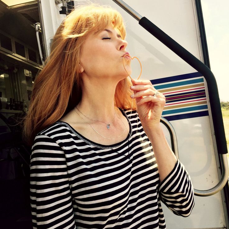 a woman standing in front of a bus blowing her nose to the side while looking up