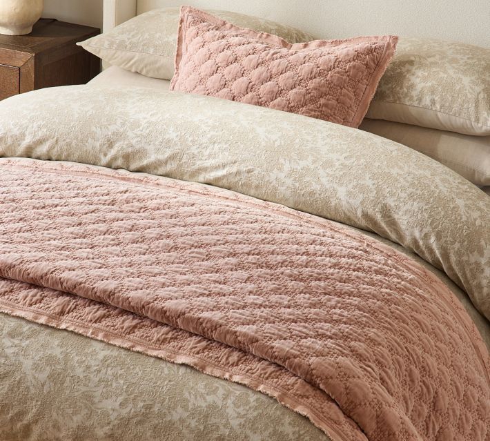 a bed with pink and beige comforters on top of it next to a night stand