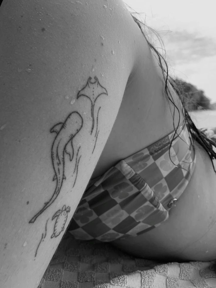 a woman laying on top of a beach with a tattoo on her arm and chest