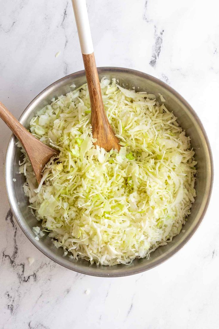 shredded green vegetables in a silver bowl with wooden spoons on a marble countertop