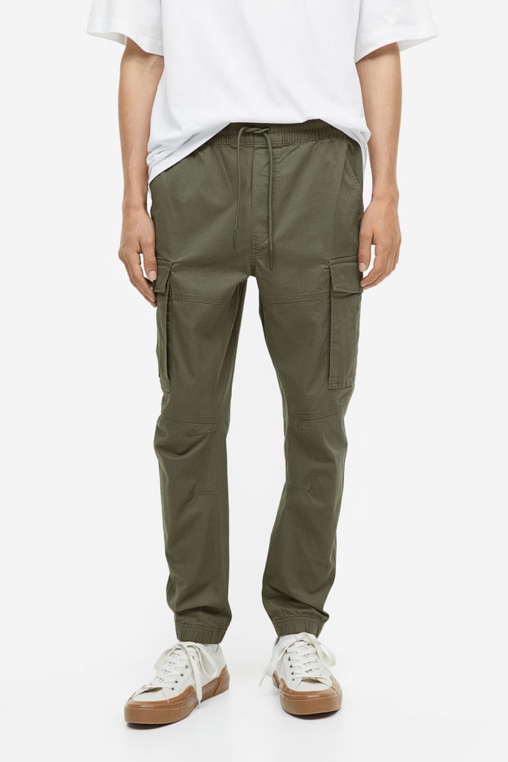 Joggers in woven cotton fabric. Waistband with drawstring and covered elastic. Diagonal side pockets  back pockets with flap and concealed snap fasteners  and leg pockets with flap and concealed snap fasteners. Tapered legs with seams and darts at knees and covered elastic at hems. Military Style Cotton Bottoms With Elastic Waistband, Urban Cargo Jeans With Elastic Waistband, Urban Straight Leg Cargo Jeans With Elastic Waistband, Military Style Cotton Cargo Pants With Elastic Waistband, Casual Cargo Pants With Patch Pockets, Military Cotton Cargo Pants With Elastic Waistband, Utility Style Cotton Cargo Jeans With Elastic Waistband, Utility Cotton Cargo Jeans With Elastic Waistband, Military Style Relaxed Fit Cargo Pants With Elastic Waistband