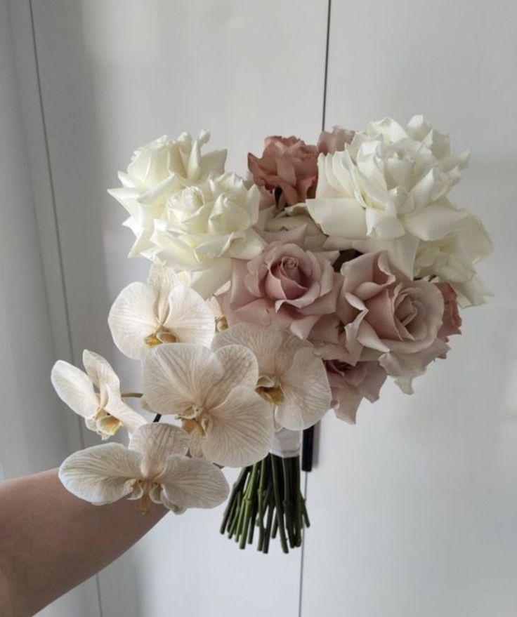 a hand holding a bouquet of flowers in front of a white wall with mirrors behind it