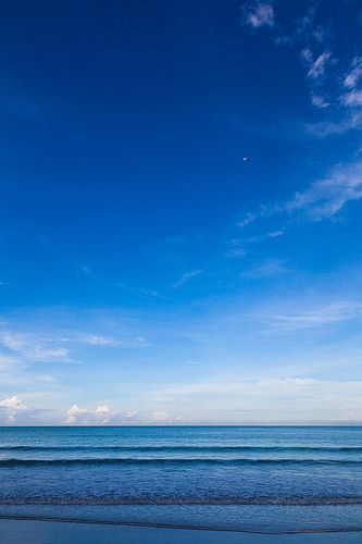 two people walking on the beach with surfboards in their hands, under a blue sky