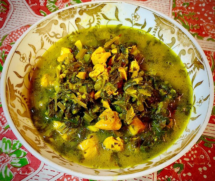 a white bowl filled with green soup on top of a red and gold table cloth