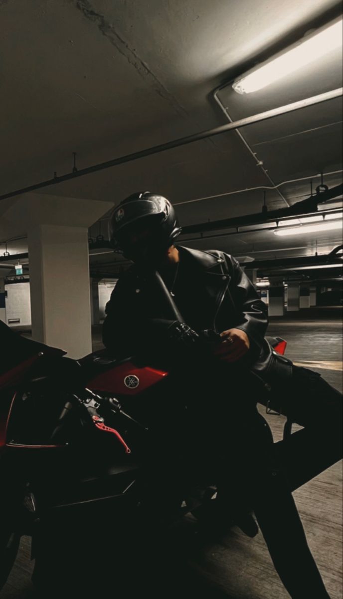 a man riding on the back of a red motorcycle in a parking garage next to a building