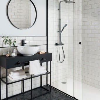 a black and white bathroom with a sink, mirror, shower stall and towel rack